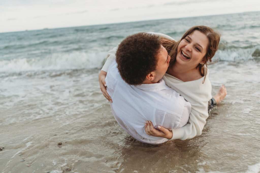 A couple joyfully barrel rolls through the water at their engagement session