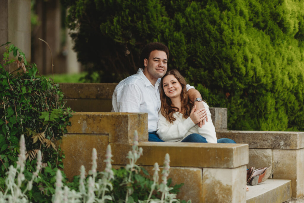 A couple poses sitting down on the staircase, with their arms wrapped around each other for Harkness Memorial State Park photos in the gardens.