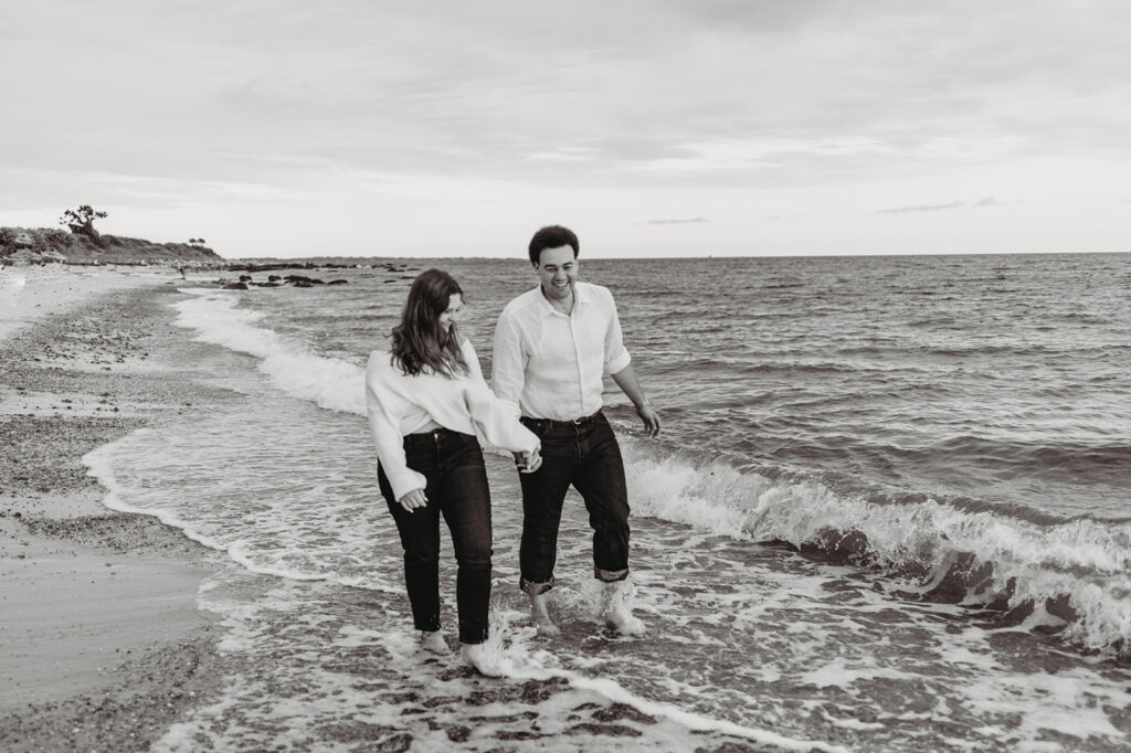 man and woman walk through the water at the beach