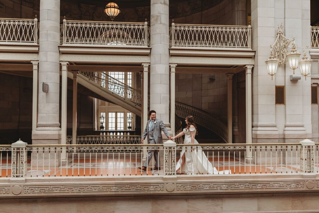 groom leads bride by the hand walking through the halls of Hartford City Hall