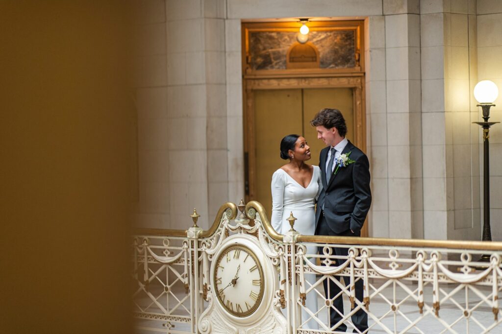 couple posing by railing with clock before their hartford city hall wedding