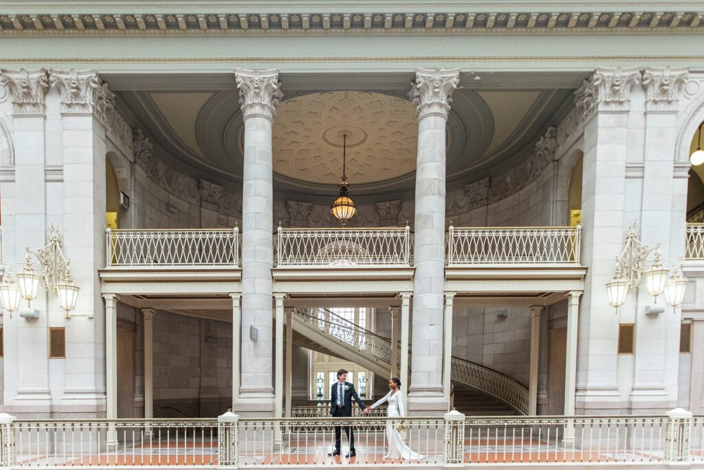 groom leads bride by the hand walking through the halls of Hartford City Hall