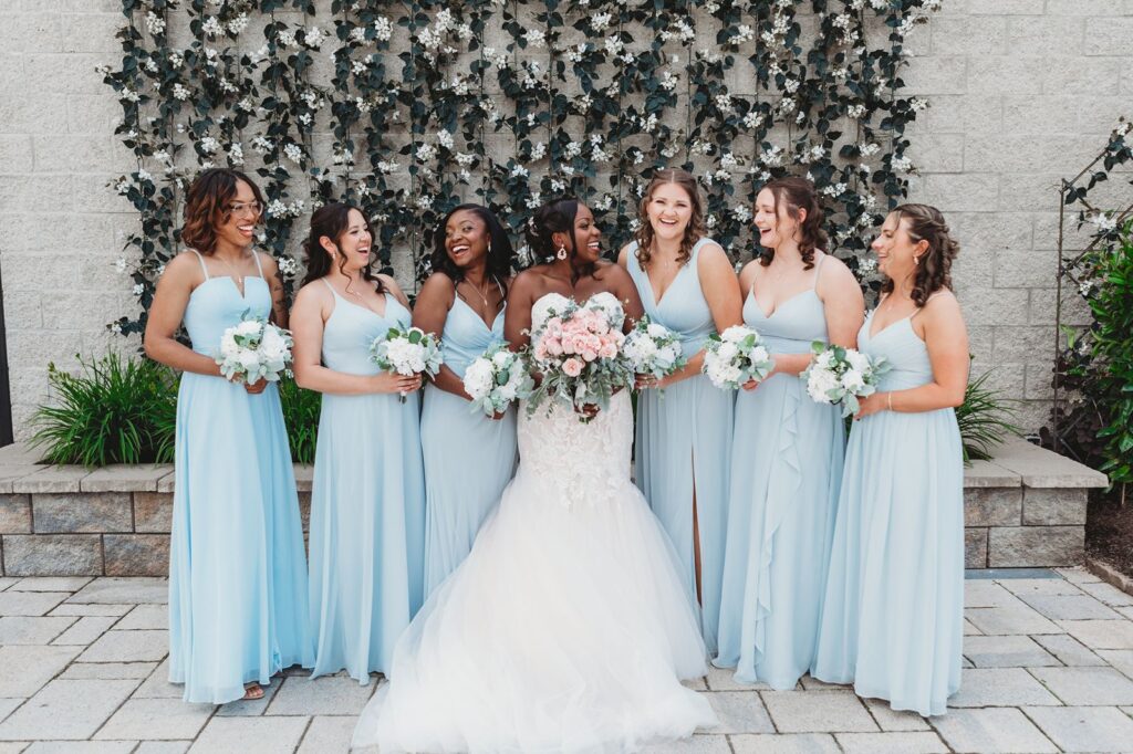 A bridal party poses in front of stonework and foliage.