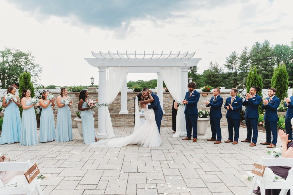 First kiss at a wedding ceremony with a beautiful sky backdrop.