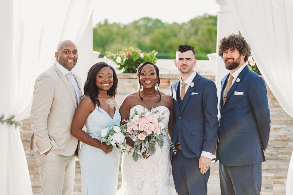 A couple poses with some family for a photo under the ceremony arbor and a light flare created a rainbow in the photo.