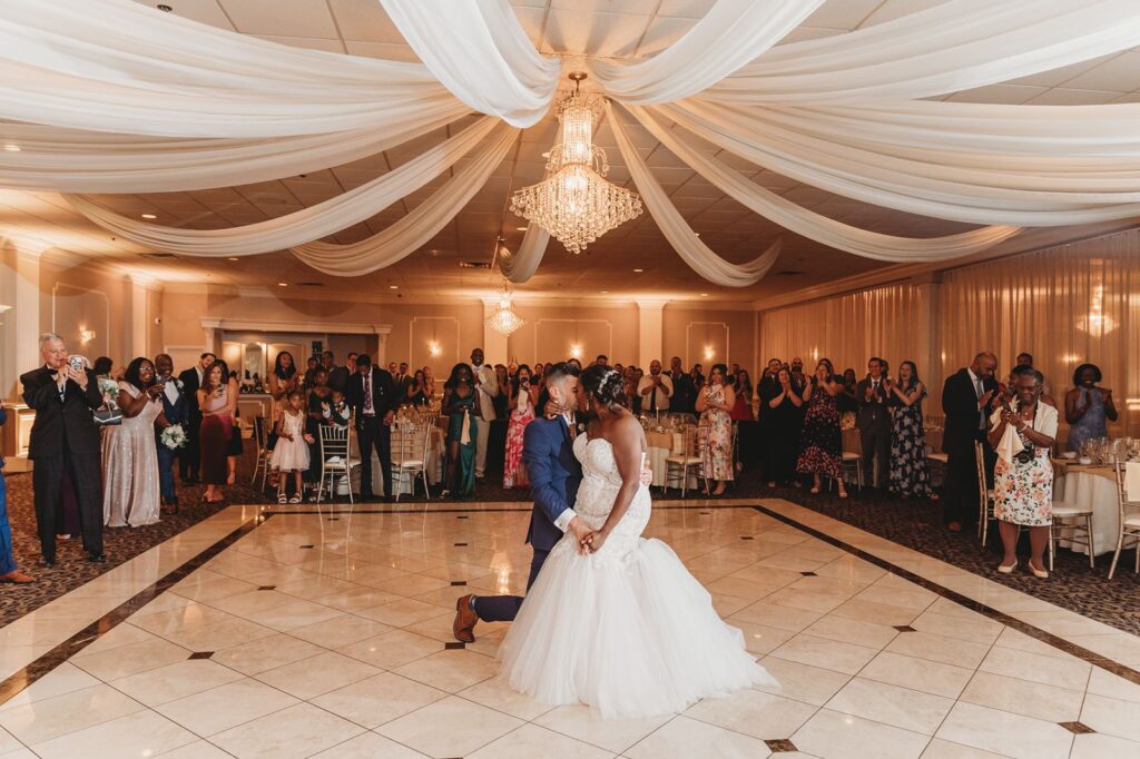 A bride sits on her husband's knee for the end of their first dance.