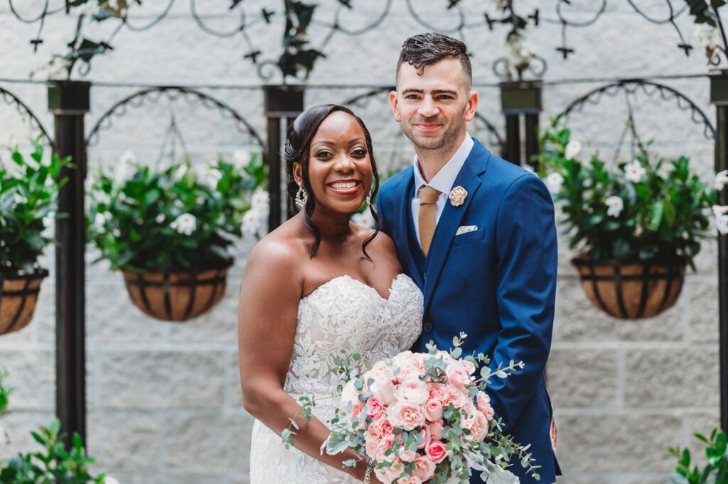 Bride and groom smiling for a formal portrait under a wrought iron pergola with flowers at La Bella Vista in Waterbury.