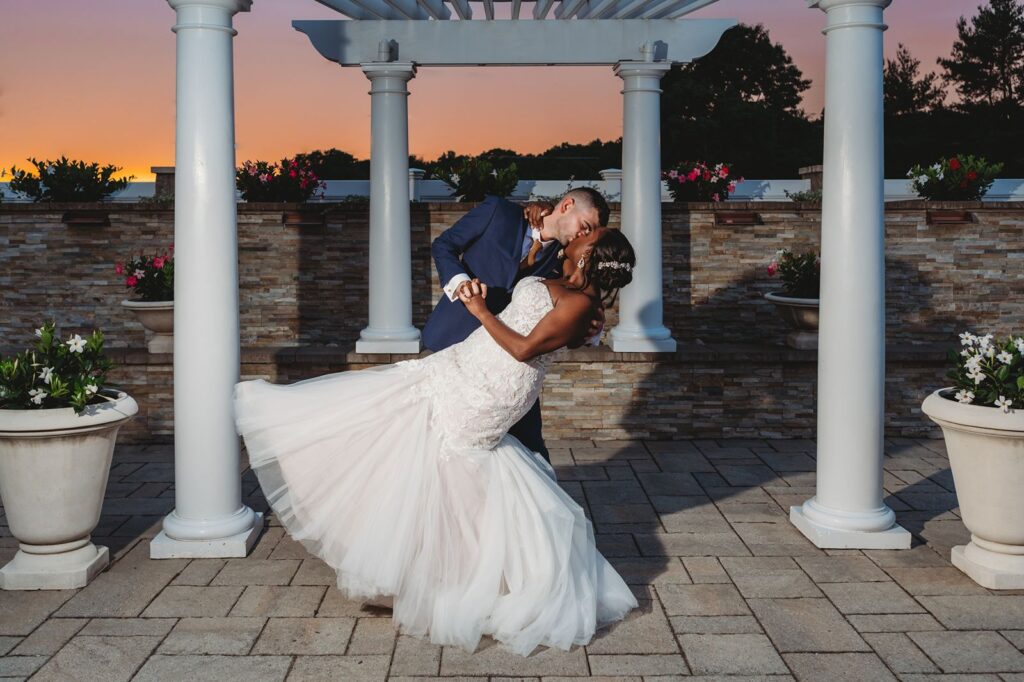 Bride and groom kissing and doing a dip under the white pergola at La Bella Vista in waterbury.