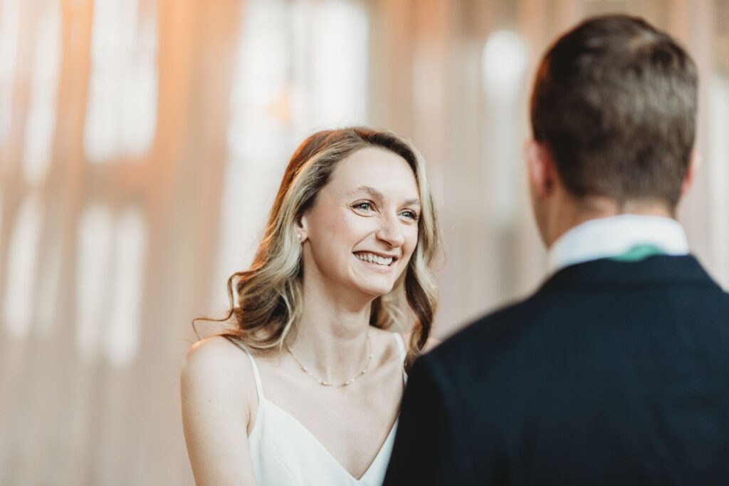bride smiling from ear to ear with joy backlit by large windows of the lace factory