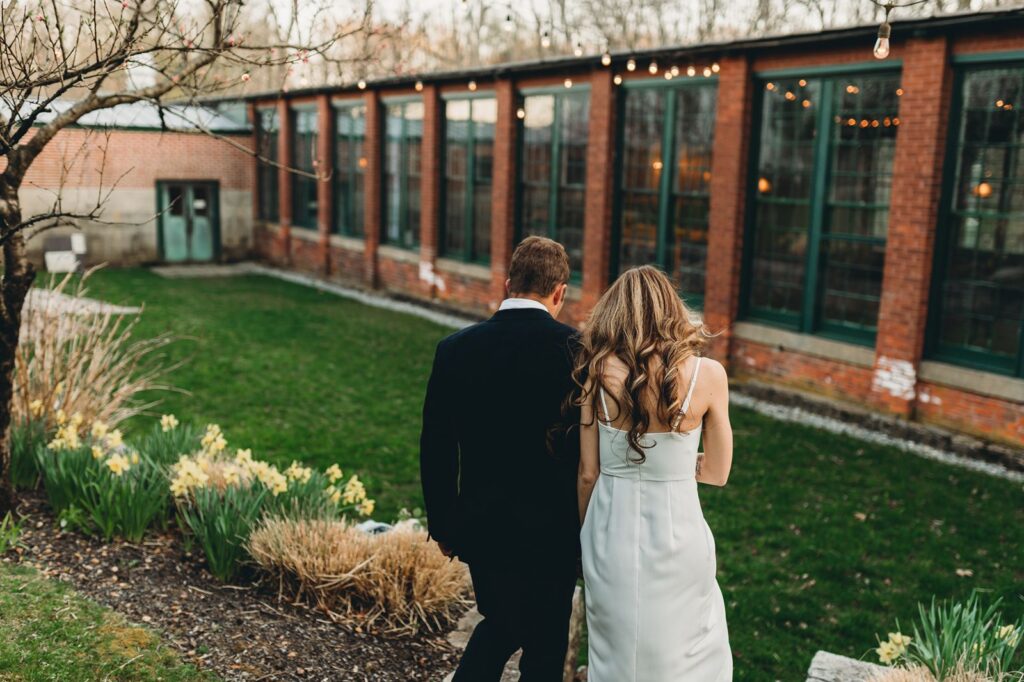 Outside view of couple walking toward green grass and tall industrial windows