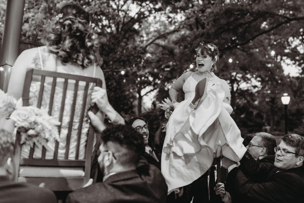 Bride laughing and shrieking in joy as she is carried for the Jewish Hora traditional at Queens Botanical Garden Reception