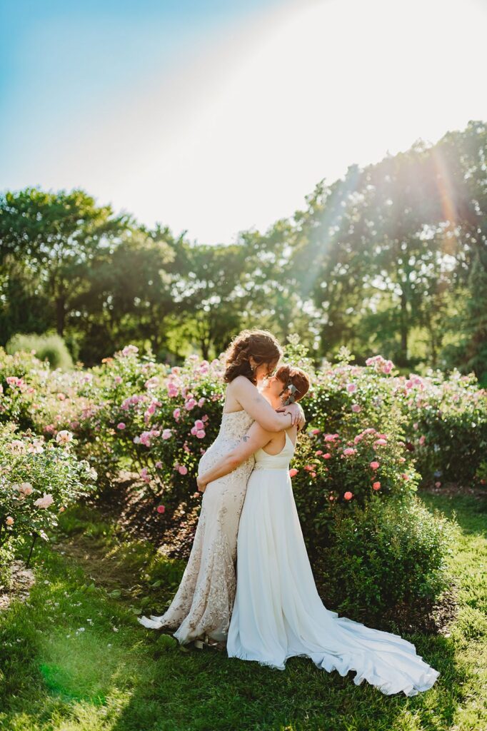 One partner picks their wife up in front of the rose garden and blue sky