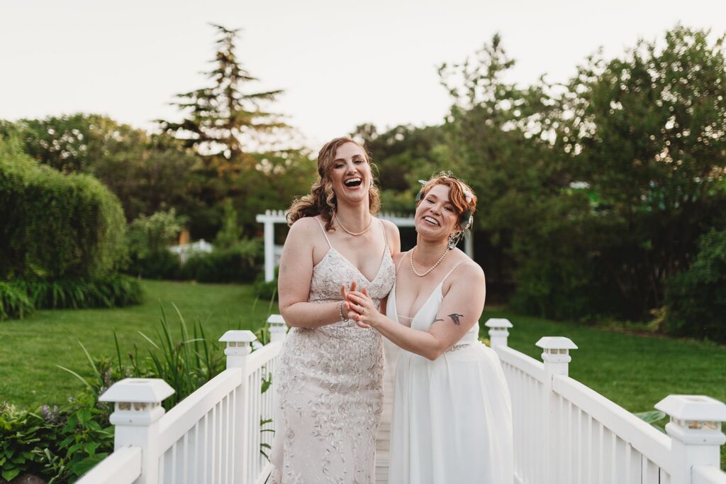 brides on a bridge with white picket fence sides expressing joy