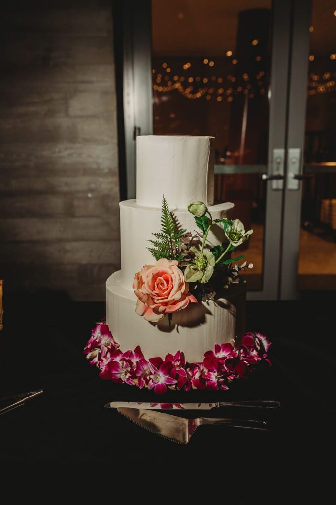 a white three tier wedding cake with orchids and a rose adorning it