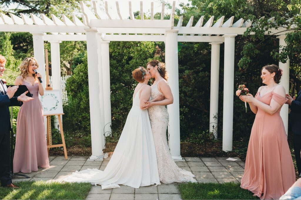 couple shares their first kiss under the arbor of the ceremony space at Queens Botanical Garden