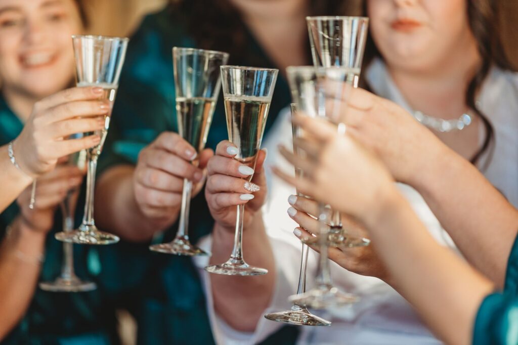 bride and bridesmaids in robes doing a champagne toast and faces are not visible only hands