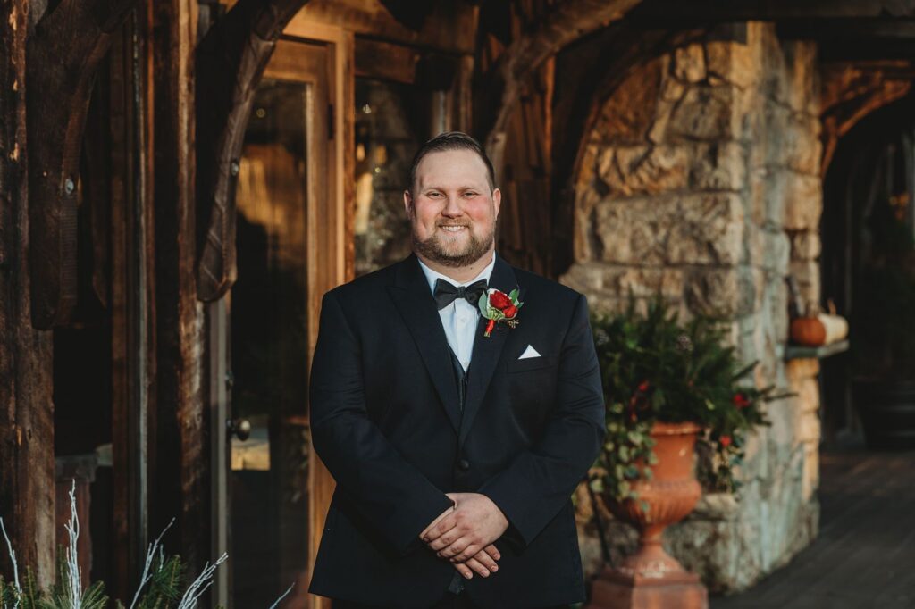 groom with black bowtie, red rose boutonniere and suit posing behind Bill Miller's Castle stone wall